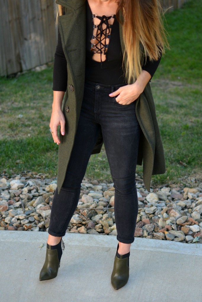 Ashley from LSR in a sleeveless military peacoat, a lace-up bodysuit, black Madewell jeans, and olive stiletto booties