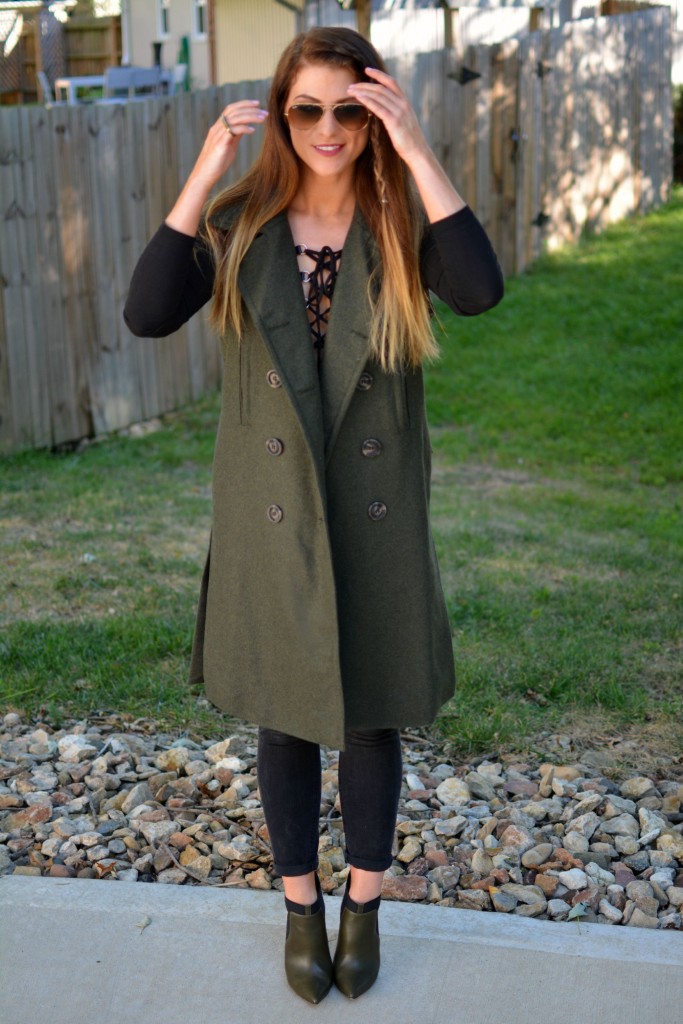 Ashley from LSR in a sleeveless military peacoat, a lace-up bodysuit, black Madewell jeans, and olive stiletto booties