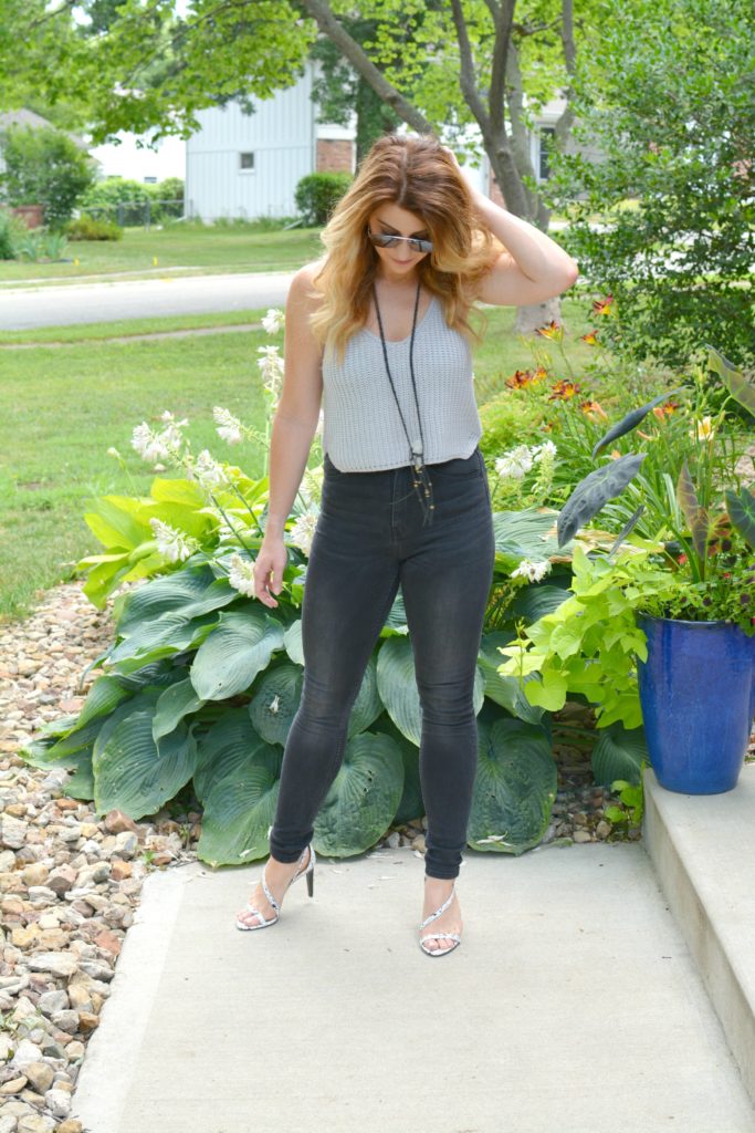 Ashley from LSR in a cropped gray sweater tank, black jeans, and white marble sandals