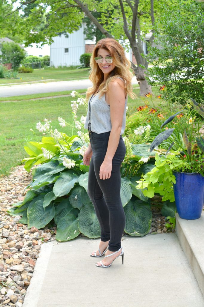 Ashley from LSR in a cropped gray sweater tank, black jeans, and white marble sandals