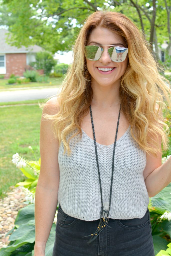 Ashley from LSR in a cropped gray sweater tank, clear quartz necklace, and mirrored sunglasses