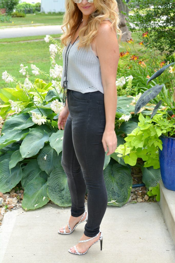 Ashley from LSR in a cropped gray sweater tank, black jeans, and white marble sandals