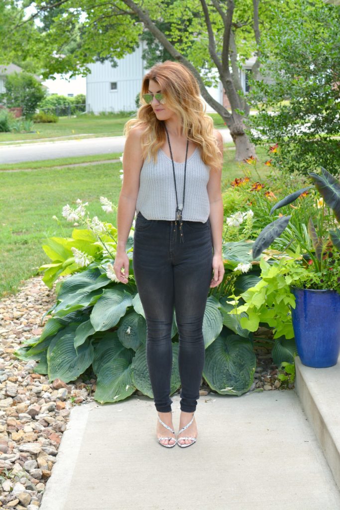 Ashley from LSR in a cropped gray sweater tank, black jeans, and white marble sandals