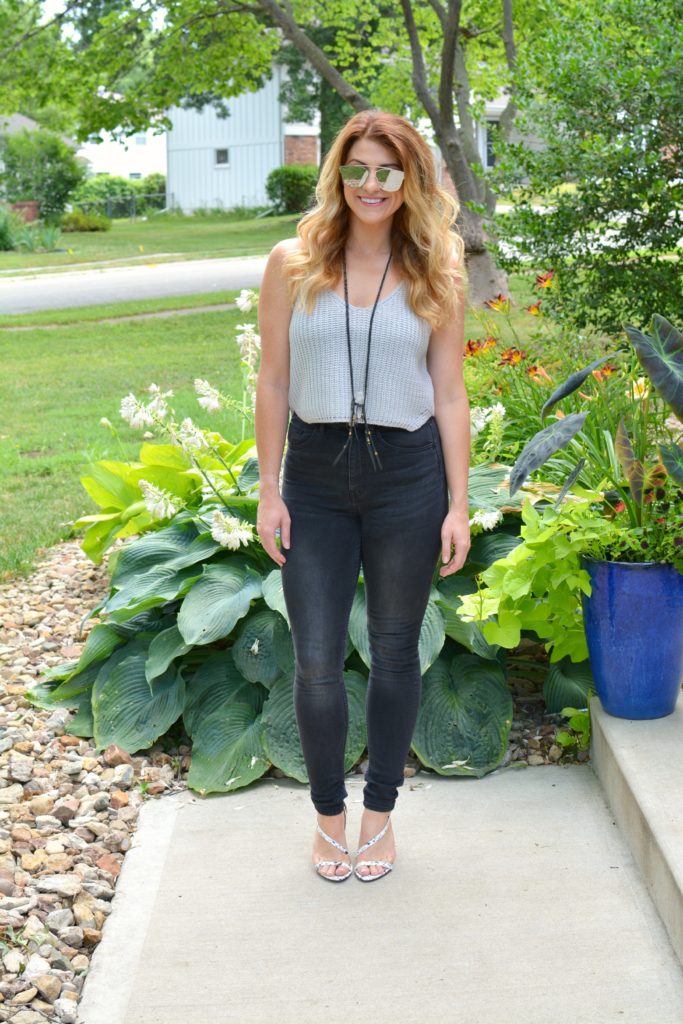 Ashley from LSR in a cropped gray sweater tank, black jeans, and white marble sandals