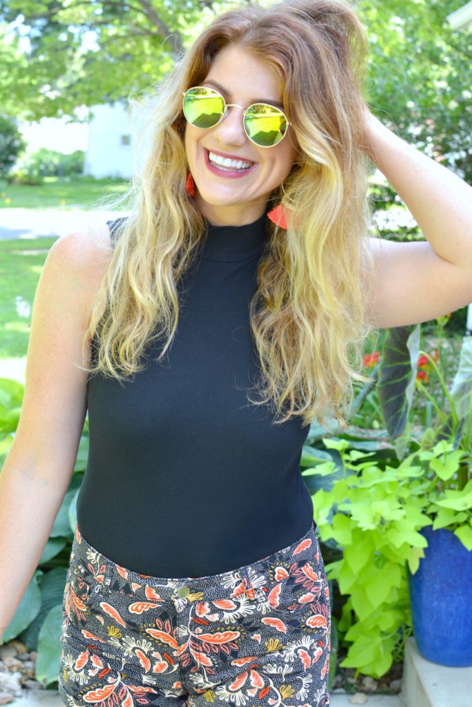 Ashley from LSR In a black bodysuit, printed shorts, and round mirrored sunglasses