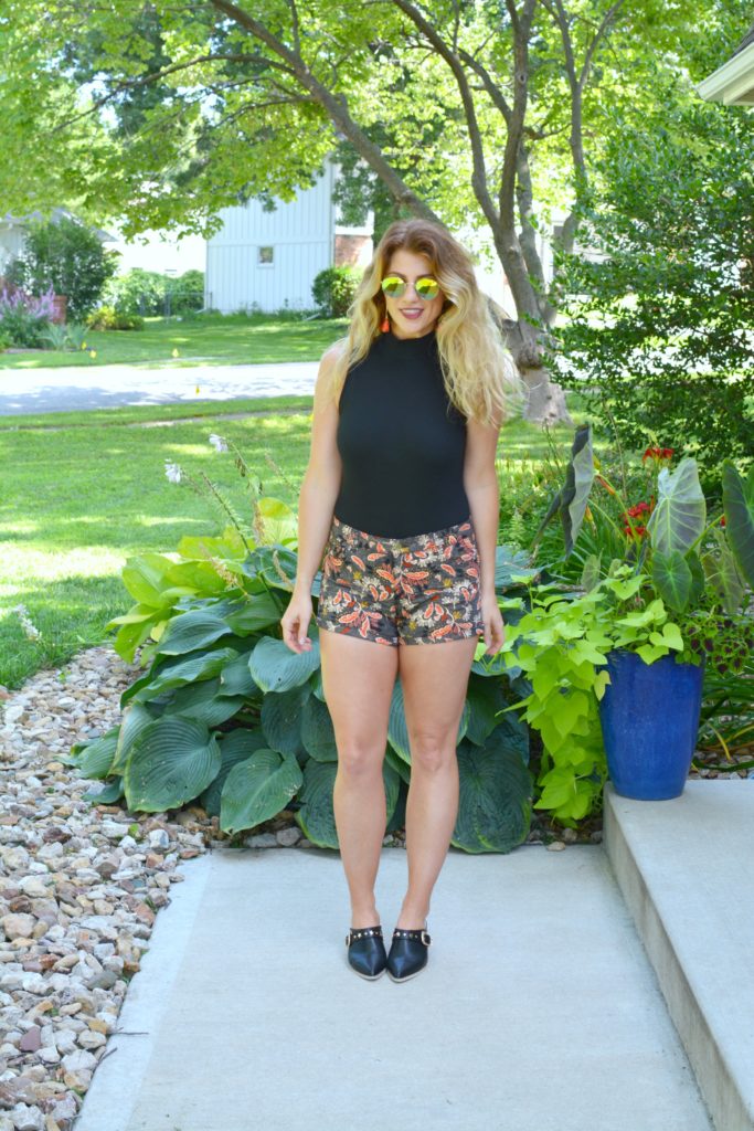 Ashley from LSR In a black bodysuit, printed shorts, and black leather mules