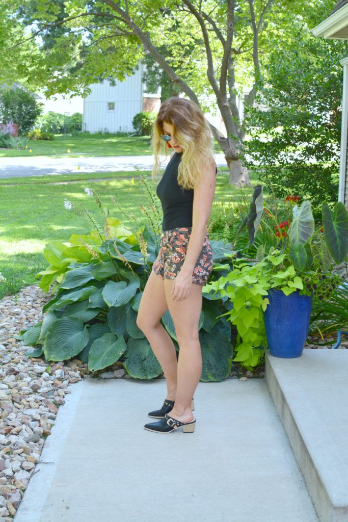 Ashley from LSR In a black bodysuit, printed shorts, and black leather mules