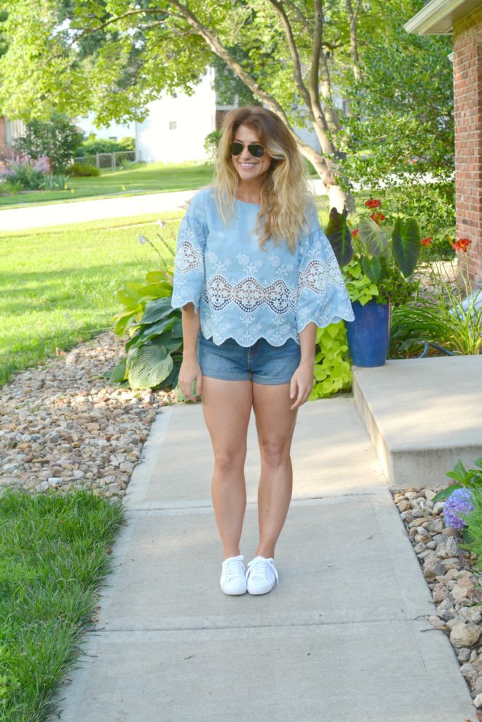 Ashley from LSR in a chambray and lace blouse, denim shorts, and white sneakers