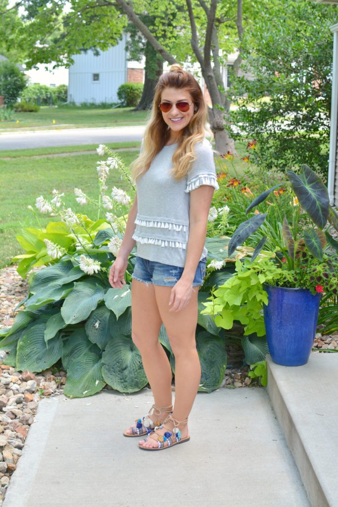 Ashley from LSR in a gray tassel tee, cutoff shorts, and pom pom lace-up sandals
