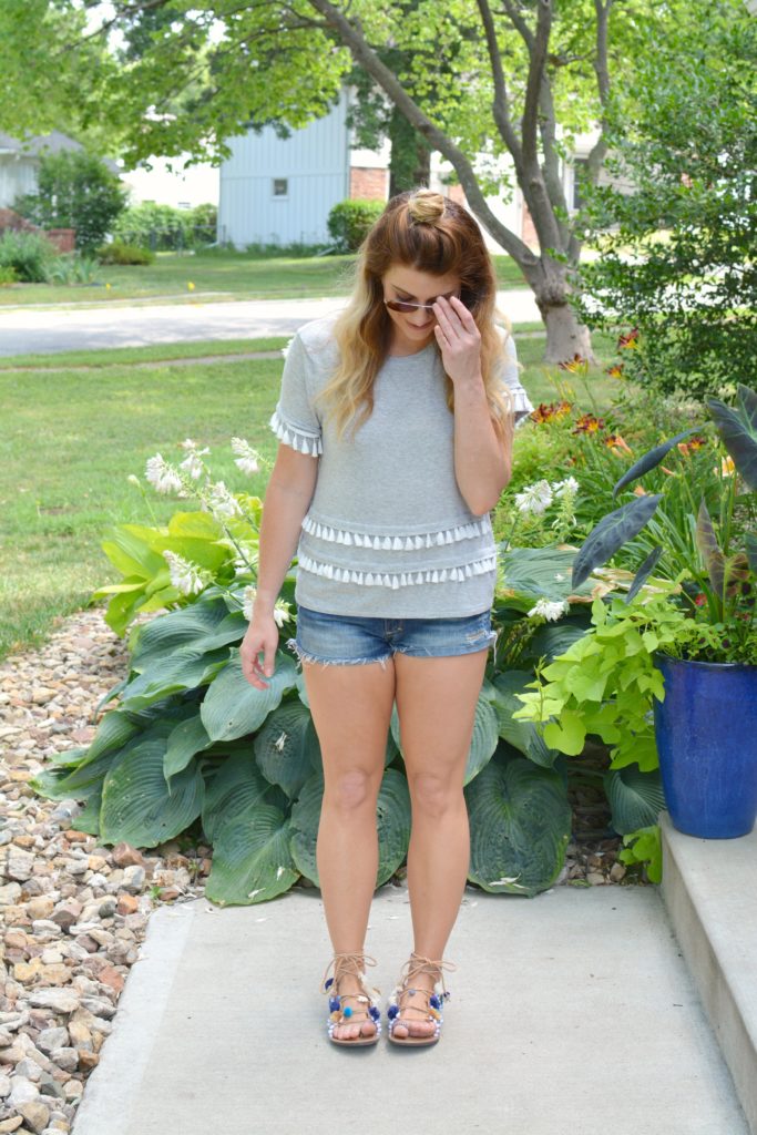 Ashley from LSR in a gray tassel tee, cutoff shorts, and pom pom lace-up sandals