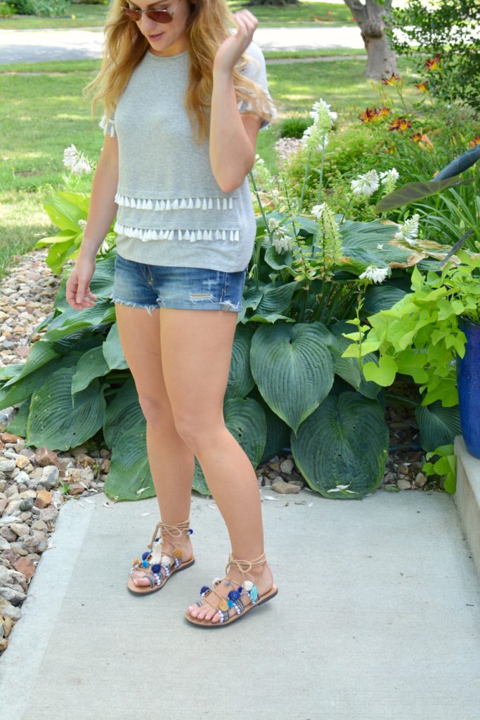 Ashley from LSR in a gray tassel tee, cutoff shorts, and pom pom lace-up sandals