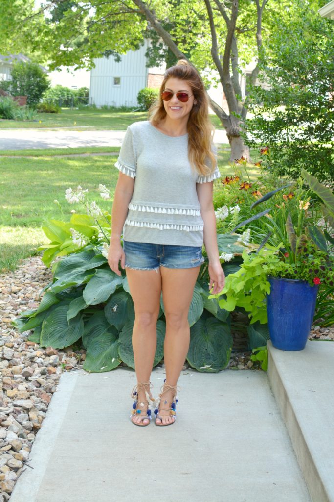 Ashley from LSR in a gray tassel tee, cutoff shorts, and pom pom lace-up sandals