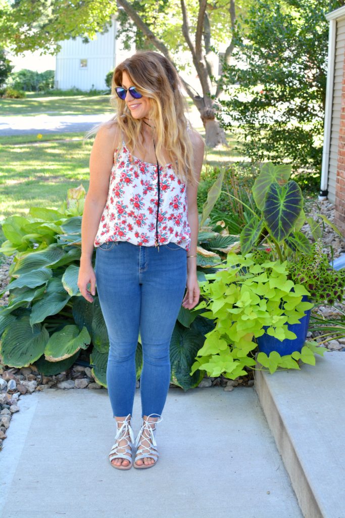 Ashley from LSR in a floral tank, stepped hem jeans, and white lace-up sandals