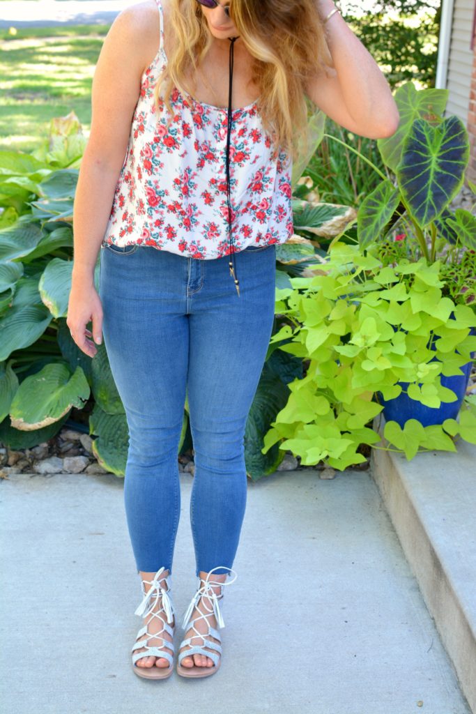 Ashley from LSR in a floral tank, stepped hem jeans, and white lace-up sandals