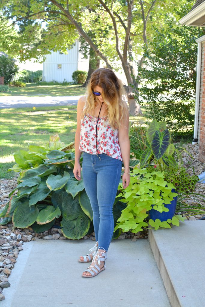 Ashley from LSR in a floral tank, stepped hem jeans, and white lace-up sandals