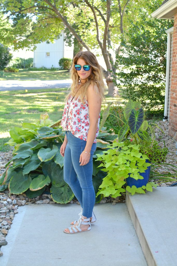 Ashley from LSR in a floral tank, stepped hem jeans, and white lace-up sandals