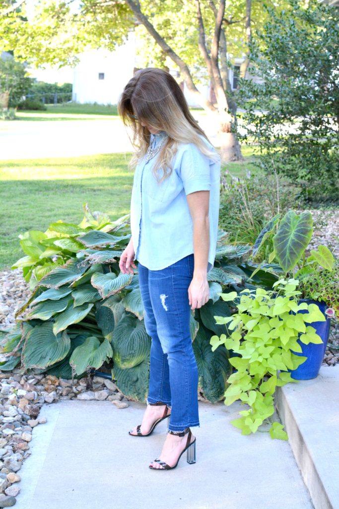Ashley from LSR in a light chambray shirt, raw hem jeans, and lucite heels with a statement necklace