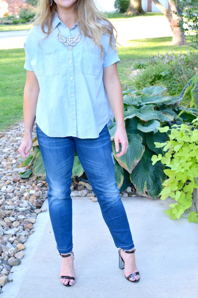 Ashley from LSR in a light chambray shirt, raw hem jeans, and lucite heels with a statement necklace