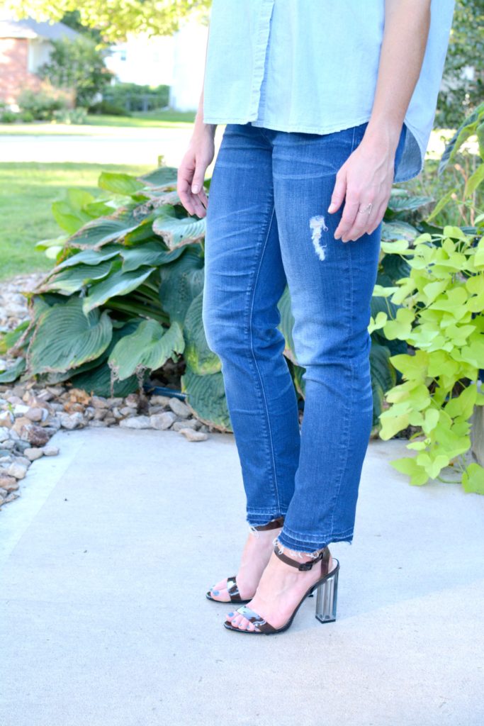 Ashley from LSR in a light chambray shirt, raw hem jeans, and lucite heels