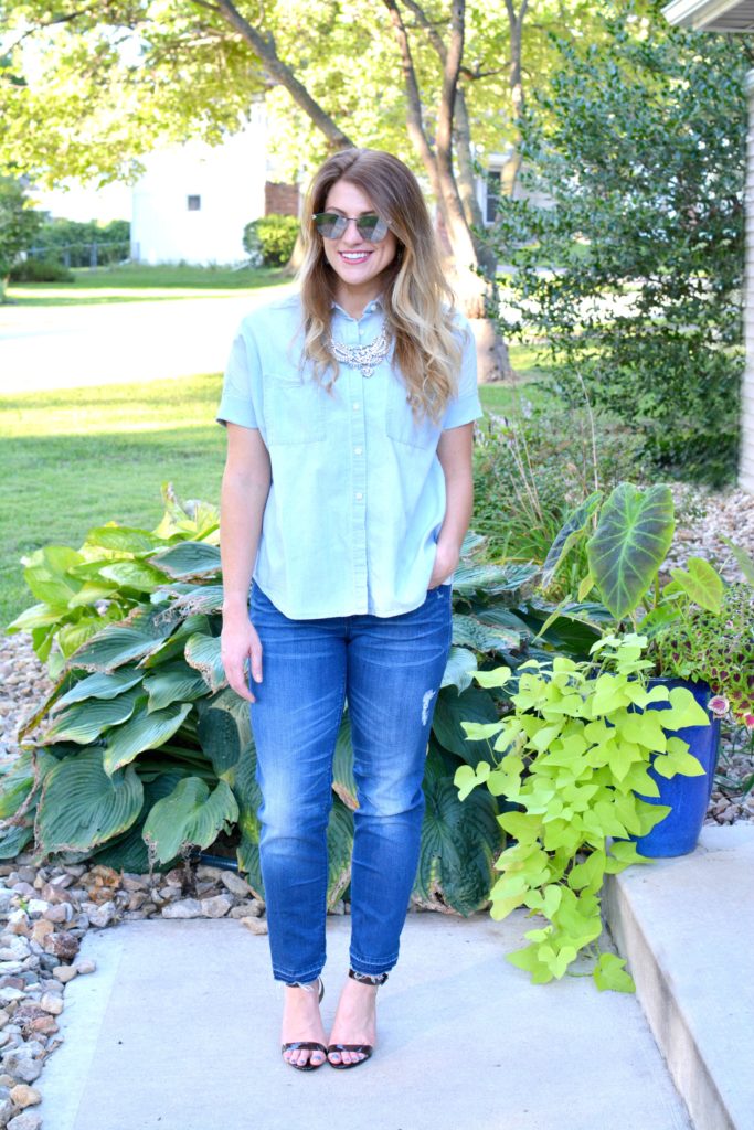 Ashley from LSR in a light chambray shirt, raw hem jeans, and lucite heels with a statement necklace